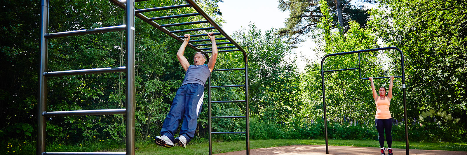 A man exercises at a park using overhead ladder bars to make his way across.